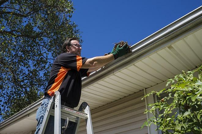 repairman using a ladder to access a damaged gutter for repair in Bronxville